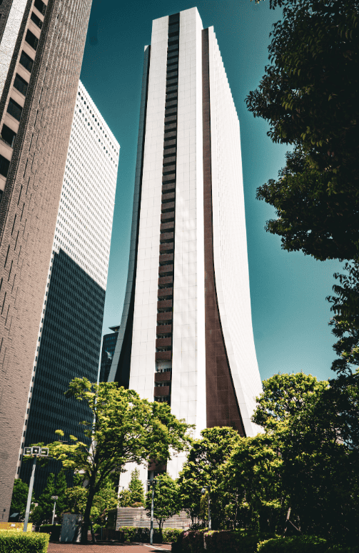 Modern city skyscraper in sunlight with surrounding greenery and trees.